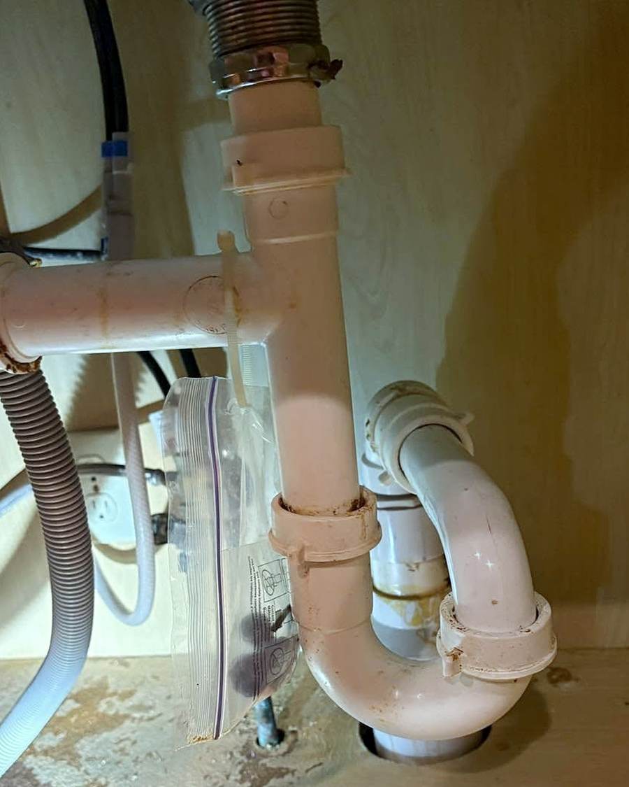 Old kitchen drain and supply lines under a cabinet in South Bend, before the repair