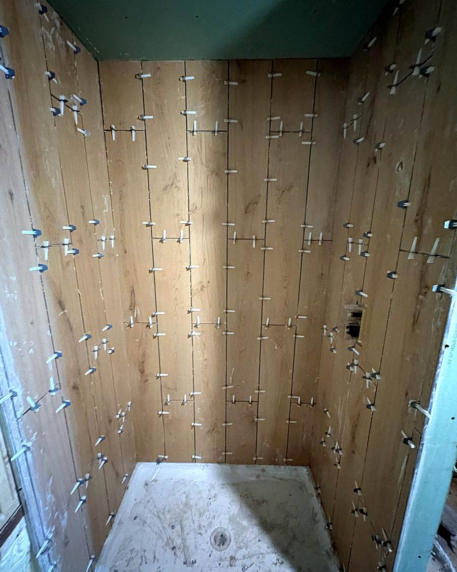 Wood-look shower wall tile in progress, held with leveling clips